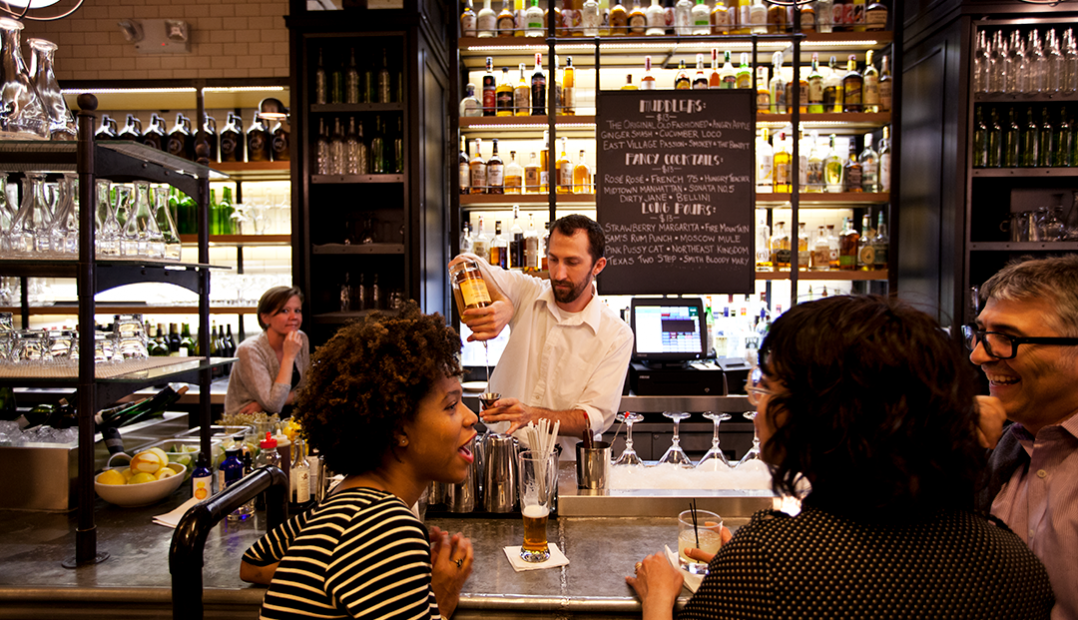 A photo of the bar at The Smith Lincoln Square with guests enjoying their drinks and the bartenders busy at work.